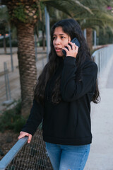 Worried young latin girl doing a phone call. Woman receiving bad news by phone. Model outdoors calling.