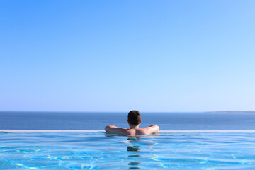 a young guy is resting on the edge of a blue pool overlooking the sea. summer vacation concept