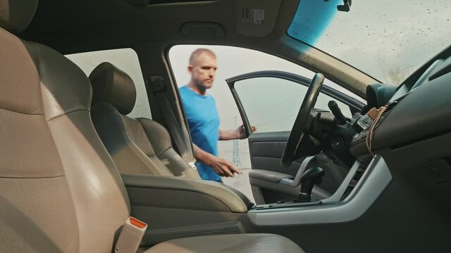 Man in lue clothes gets into car and starts it and starts driving. Bad weather outside