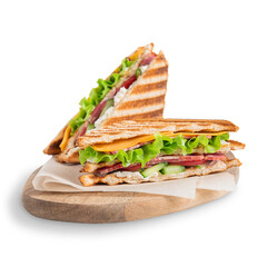 Two homemade sandwiches consisting of cucumber, slice of meat and cheese, lettuce and tomatoes between slices of grilled bread served on cutting board with cooking paper isolated on white background