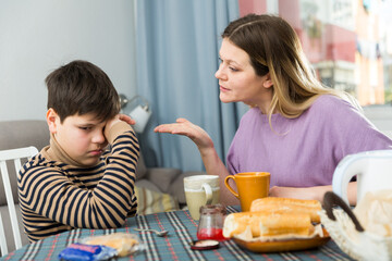 Upset mother and unhappy son arguing during breakfast in domestic interior