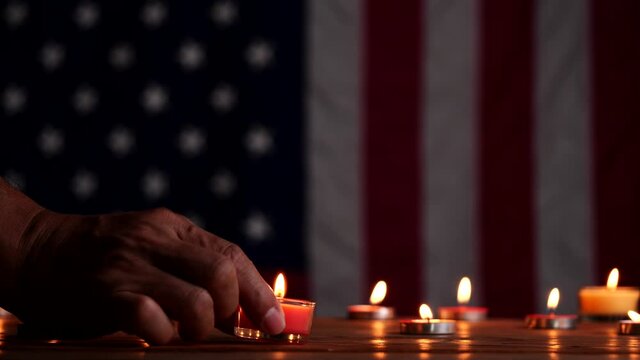 Memorial Day, Man hand put a burning candle on wooden table for honoring and mourning with American flag background. Concept of Memorial Day or 4th of July,Independence Day,Veterans Day, USA flag.