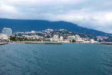 Fototapeta premium Windy weather by the sea, on the shore on a large stone a man sits alone. A person gets relaxation on the beach, communicating in one with nature.