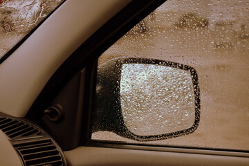 view in the side mirror from the inside of the car with rain on the glass