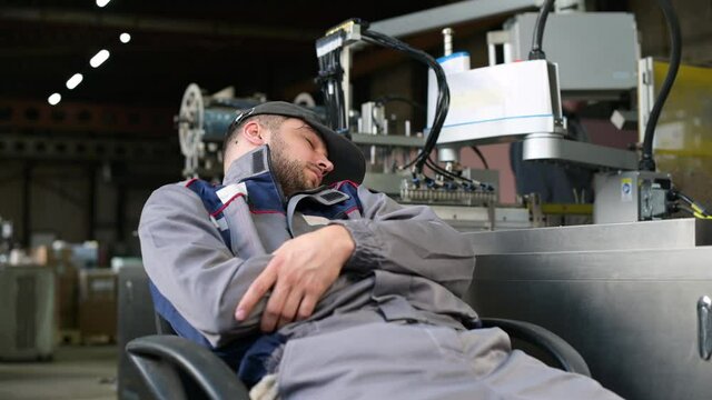 A production technician sleeps near an assembly line, violating safety precautions. Exceeding labor standards and mental overload leads to fatigue
