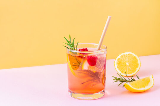 Trendy exotic summer drink with disposable paper straw and rosemary on bicolor background (pink and orange). Fresh fruit lemonade with raspberry for vegans. Copy space