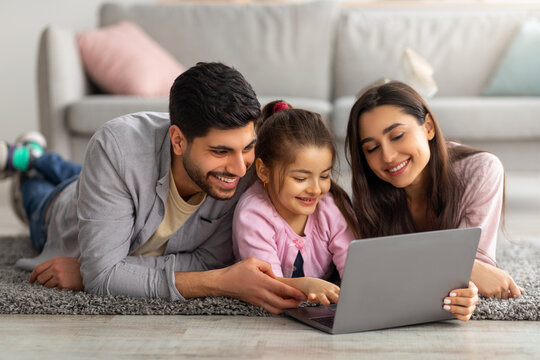 Family Weekend. Cheerful Arab Parents Teaching Their Little Daughter Using Laptop, Spending Time At Home Together