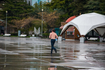 Morning. An area with puddles after rain. A man with a naked torso is jogging in the morning. The concept of a healthy lifestyle, sports and proper nutrition.