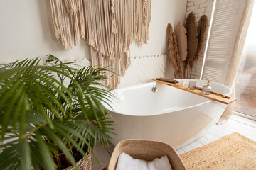 Cozy bathroom interior with big bathtub, plant and rustic decoration