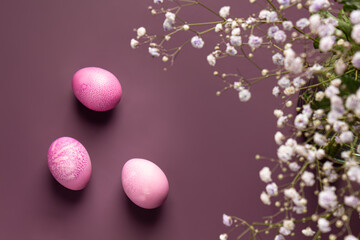 Obraz na płótnie Canvas Dyed pink easter eggs with beautiful flowers on a purple background.
