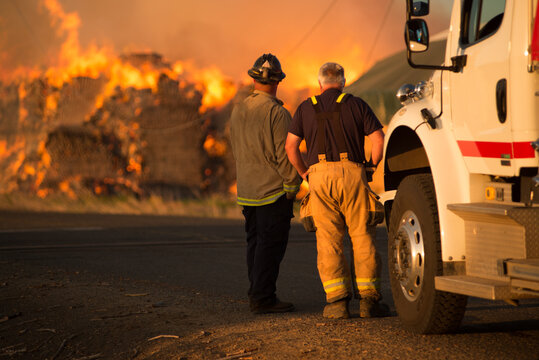 firefighter watching burning blaze of haystack bales on fire in agricultural field lower yakima valley washington state