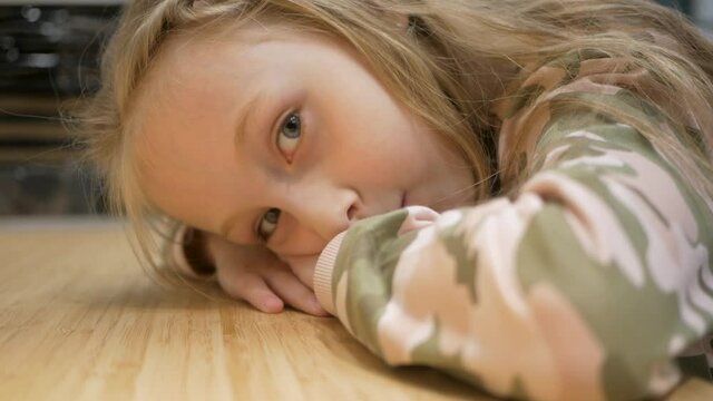 portrait of a little girl. The girl put her hands under her head and lies on the table.