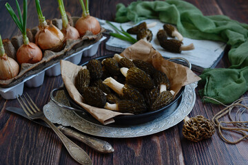 Fresh morel mushrooms on a plate and green onions on a wooden background, close-up. The first spring mushrooms