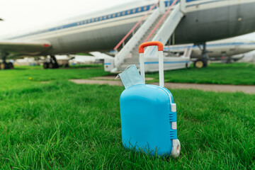 Suitcase with protective face mask in front of the plane in airport