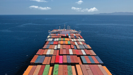 Aerial drone view above huge colourful container carrier vessel cruising deep blue open ocean sea