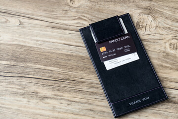 The black credit card on blank bill paper in  leather black bill receipt. Receipt Holder with credit card on cafe or Restaurant. 