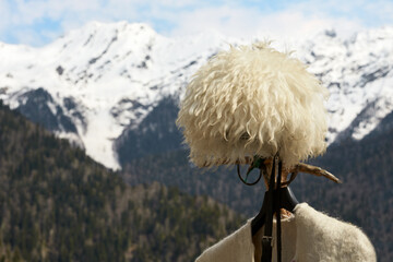 A mountain hat made of white sheep wool and a fragment of a felt cape on the background of...
