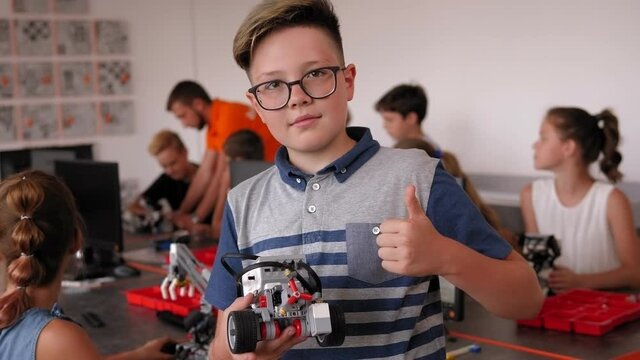 A small smart boy holds a robot in his hands in the robotics office.
