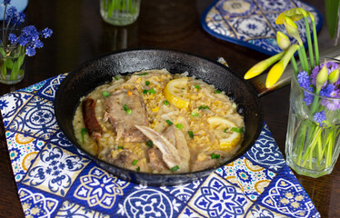 Stew of chicken, lentil, lemon, spices in pan on blue textile cover on brown wooden table and flowers in vases