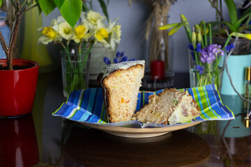 still life with Easter cake pieces in plate, yellow and blue flower bouquets in vases, home plants in pots on wooden table and blue  background