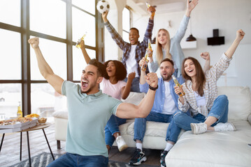 Group of young multiracial friends watching soccer game on TV with snacks and beer, cheering for favorite team at home