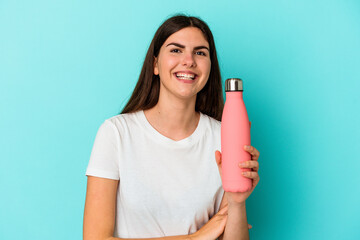 Young caucasian woman holding water bottle isolated on blue background laughing and having fun.