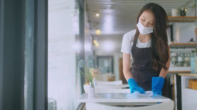 Close-up.Asian female worker clean the table is disinfected by sprinkling with an antiseptic spray and wiping with a towel cloth for protect coronavirus. reopening cafeteria or restaurant
