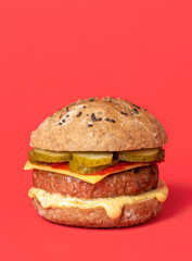 Veggie burger with plant-based cheese and meat, isolated on a red background.