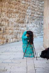 young girl in a long green dress takes pictures with a tripod in the old city