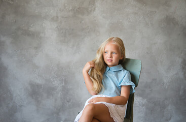 Girl is sitting on a chair and grimacing. Photo is great for demonstrating the character of a child - stubbornness, harmfulness, cunning, coquetry.