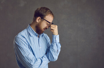 Side profile view studio shot of tired young man suffering from computer eye strain rubbing sore...