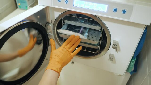 Laboratory worker putting medical instruments into steam autoclave sterilization machine, disinfection in a dental clinic