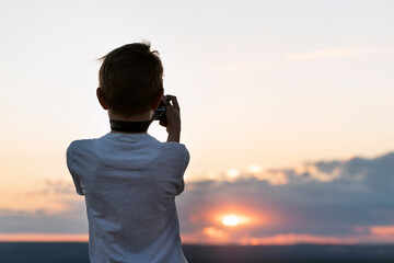 Fototapeta premium Boy photographs the sunset. Child with camera on setting sun background. Rear view
