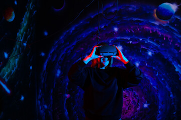 Emotional happy girl in modern virtual reality glasses with neon red and blue light on the background of space in the playroom. VR headset concept