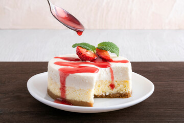 Cheesecake is poured over with berry syrup. Dessert garnished with fresh strawberries.