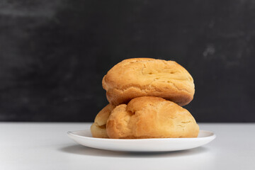 Profiteroles on white plate. Homemade puffs, popovers and eclairs. Side view