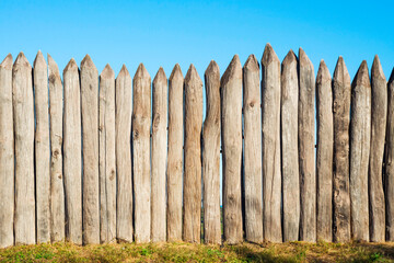 Wooden fence from logs on a background of blue sky.  Pointed logs, old wooden fence
