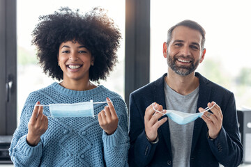 Multiethnic business people taking off an hygienic mask while smiling while looking at camera in the office.