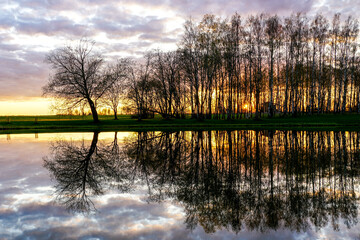 wonderful sunset view on the lake shore with tree reflections in the water