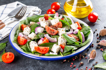 Fresh vegetables salad from spinach, tomato, feta cheese, onion in plate on a dark background