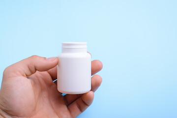 Hand holding white open bottle of pills against blue background. Medicine concept