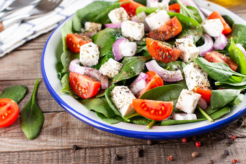 Spinach salad with fresh tomato, red onion and feta cheese on a wooden table. Healthy vegan food.