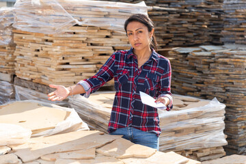 Latin American woman supervisor checking quality of natural stone tiles at hardware store warehouse