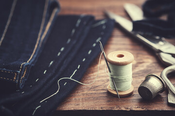 Shortening jeans. Wooden spool of  thread, thimble and scissors on table. Jeans cutting. - obrazy, fototapety, plakaty