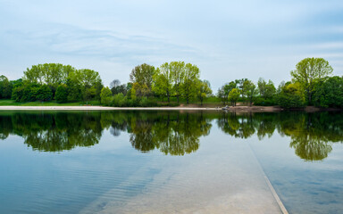 Spring landscape at lake, green trees and blue sky symmetrically reflected in water