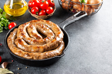 Spiral grilled sausage with spices in a frying pan on a stone background, copy space