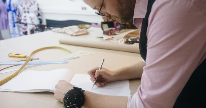 Tailor with glasses draws sewing patterns in sketchbook