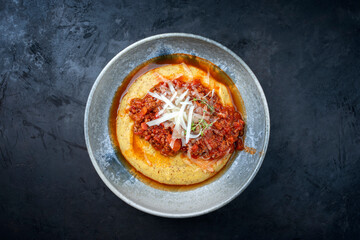 Modern style traditional Italian polenta alla sarda con salsiccia with ground meat ragu and pecorino served as top view on a Nordic design bowl with copy space