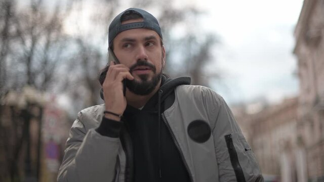 Young, modern handsome man talking on the phone on the street of a small town on a sunny spring day.