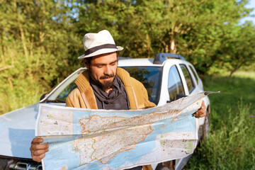 Latino man leaning on his 4wd suv car consulting on a map the route through the forest to follow. lost person with his off-road car. off-track driving. adventure concept in natural environment